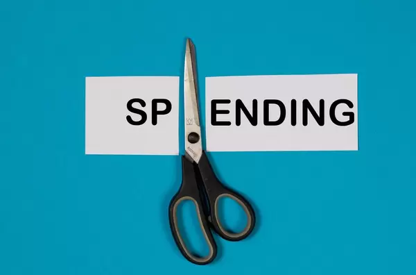 Das Wort Spending auf einem durchgeschnittenem Papier mit Schere auf blauem Hintergrund