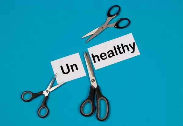 Das Wort Unhealthy auf einem durchgeschnittenem Papier mit Scheren auf blauem Hintergrund