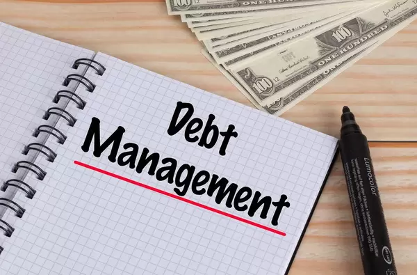Debt Management text in notebook and Dollar banknotes on wooden table