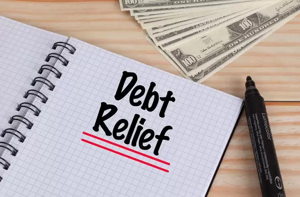 Debt Relief text in notebook and Dollar banknotes on wooden table