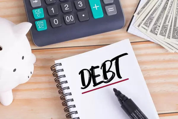 Debt text in notebook with piggy bank and calculator on wooden table