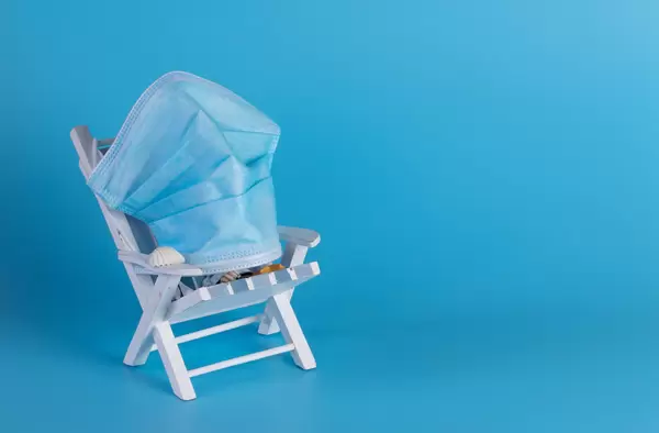 Deckchair with medical face mask on blue background