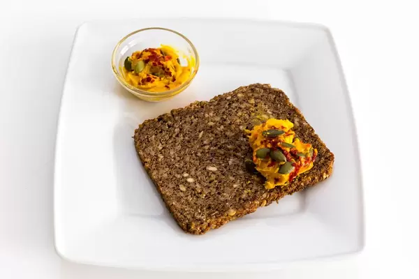 Deli Genuss - Süßkartoffelaufstrich präsentiert auf einem kernigen Vollkornbrot auf einem weißen Teller