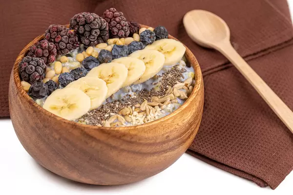 Delicious and healthy breakfast porridge with yogurt, seeds, pine nuts and fruit in a wooden bowl