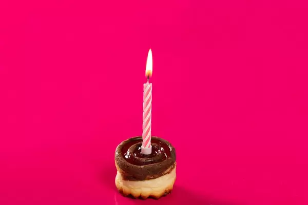 Delicious birthday cupcake with candle on pink background