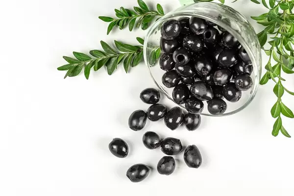 Delicious black olives with leaves on white background