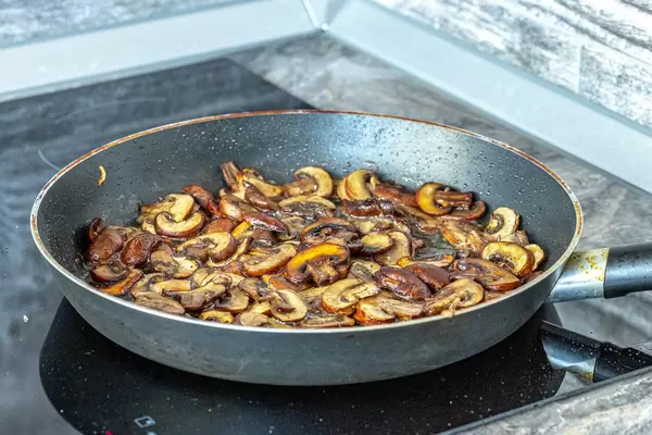 Delicious fried mushrooms in frying pan on electronic cooking surface (Flip 2019)