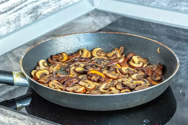 Delicious fried mushrooms in frying pan on electronic cooking surface