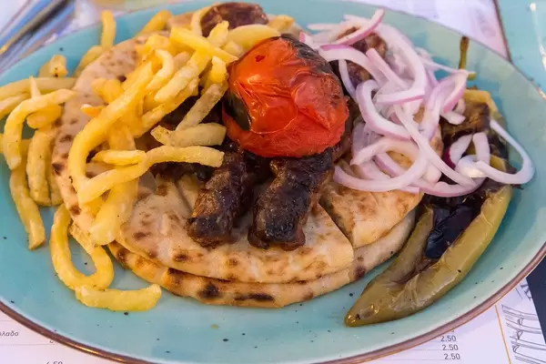 Delicious kebab pita with tomatoes from Paros, onions and grilled Greek paprika on blue plate