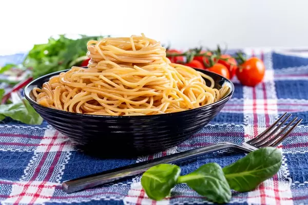 Delicious spaghetti in a black bowl with herbs and tomatoes in the background (Flip 2019)