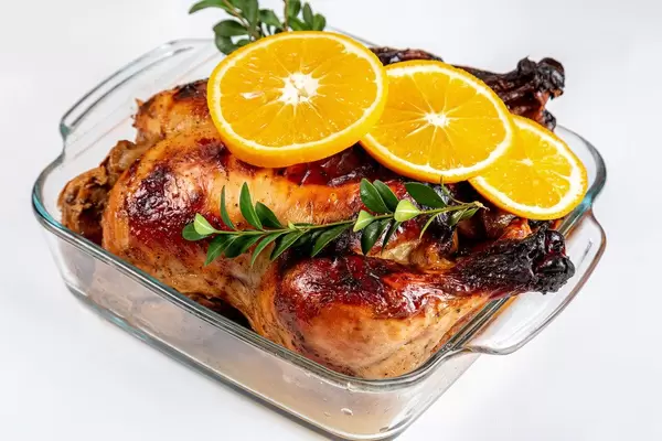 Delicious whole roasted chicken with orange in glass baking sheet, close up