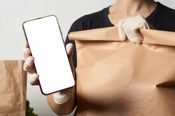 Delivery. A person in medical gloves holding a paper shopping bag and smartphone with a blank screen