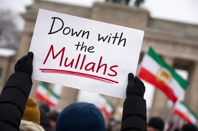 Demonstrant hält Schild mit Aufschrift 'Down with the Mullahs' vor Brandenburger Tor