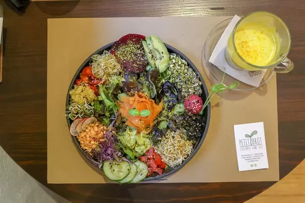 Der bunte, spanische Salat "Ensalada del Sol" neben einer Goldenen Milch im veganen Restaurant Petit Brot in Barcelona, Spanien