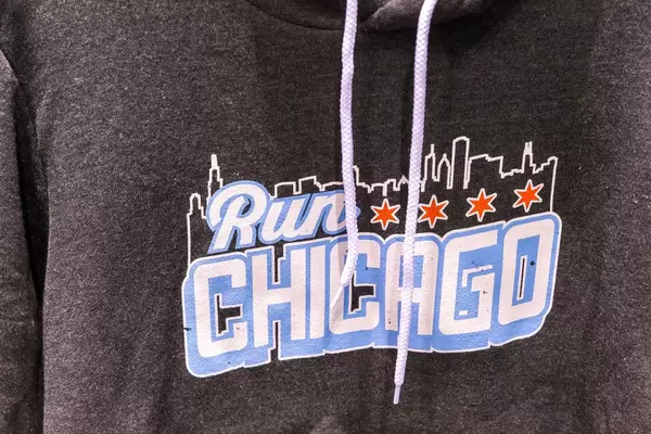 Detail of grey hoodie with "Run Chicago" graphic in white and light blue, skyline of the city and four red stars