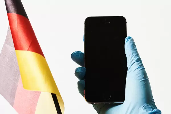 Deutsche Flagge und Hand mit Smartphone und Einweghandschuh vor weißem Hintergrund