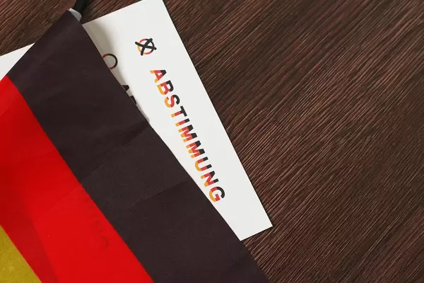 Deutsche Flagge und Zettel mit Schrift "Abstimmung" in Schwarz-Rot-Gold vor hölzernem Hintergrund