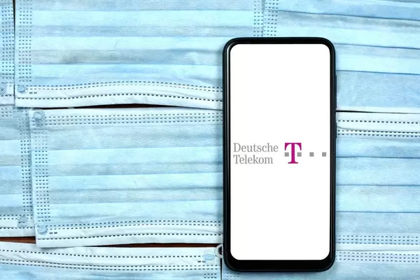 Deutsche Telekom logo on smartphone screen over the face masks. Global company during coronavirus crisis