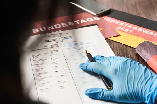 Deutsche Wählerin mit Einweghandschuh vor dem Stimmzettel für die Bundestagswahl 2021