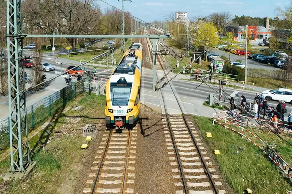 Deutscher ODEG Zug überquert einen Straßenabschnitt, während Autos und Menschen vor heruntergelassenen Schranken warten müssen