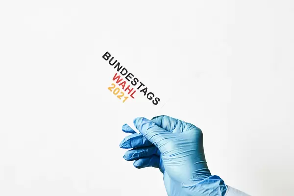 Deutschland geht wählen: Hand mit Handschuh zum Schutz gegen Corona und Zettel "Bundestagswahl 2021"