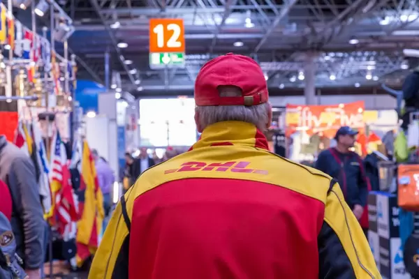 DHL-Kurier in Arbeitskleidung von hinten geht durch Messehalle