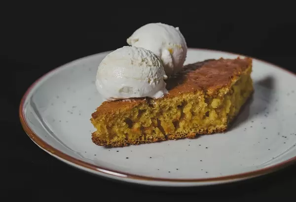 Diamantförmiger Karrottenkuchen mit zwei Eiskugeln auf einem weißen Teller angerichtet