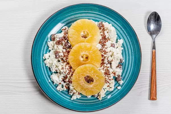 Die Ansicht von oben Close-up von Hüttenkäse mit Leinsamen, Rosinen und getrockneten Ananas Scheiben auf einem blauen Teller
