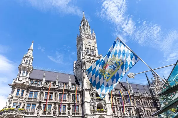 Die bayrische Landesflagge mit Regenbogenfahnen am Marienplatz im Hintergrund,  für mehr Toleranz gegenüber der LGBTQ-Community