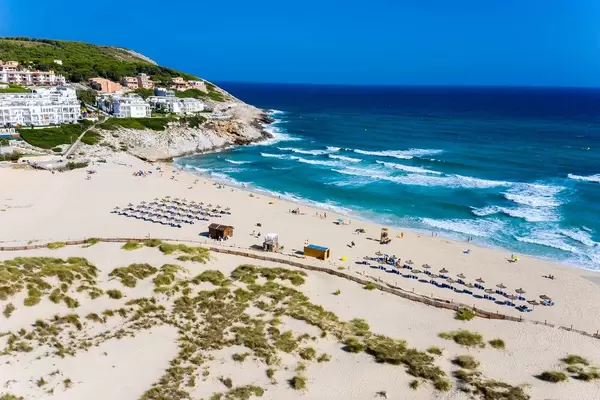Die Dünen und der Strand von Cala Mesquita auf Mallorca mit Strandschirmen aus Stroh. Luftbild