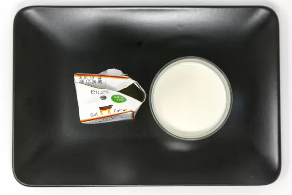 Die faire Milch - Gentechnikfreie - Deutsche Vollmilch im Glas und Verpackung auf schwarzem Teller - Aufsicht
