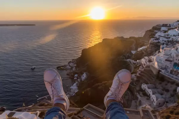 Die Füße eines Mannes, der den Sonnenuntergang beobachtet und die Aussicht auf Santorin genießt