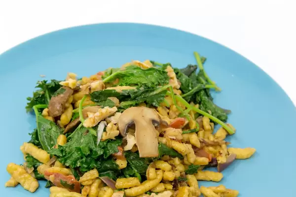 Die Hello Fresh Herbst Spätzle Pfanne mit Grünkohl, Pilzen in cremiger Soße und gerösteten Walnüssen auf einem blauen Teller in der Nahaufnahme