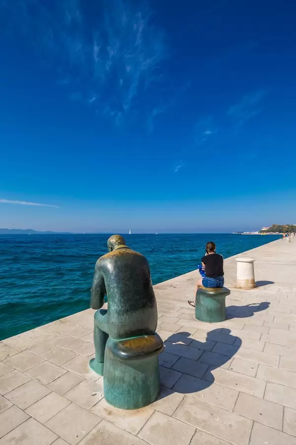 Die Kupferstatue des Spiri Brusini mit einer Muschel und eine Frau an der Promenade in Zadar