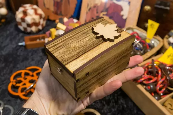 Die Rätsel Manufaktur ein Mann hält eine Holztruhe in der Hand im Hintergrund viele knifflige Handrätsel