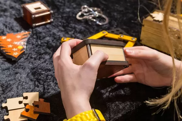 Die Rätsel Manufaktur eine Frau hält eine Holzbox in den Händen umgeben von verschiedenen Rätseln