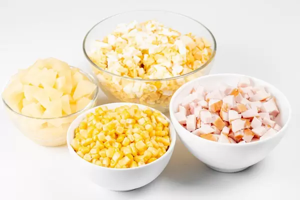 Die Zutaten in Glas- und Keramikschüsseln zur Zubereitung vom Salat mit geräuchertem Hähnchen und Ananas