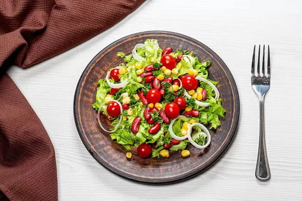 Diet salad with vegetables and red beans in a brown plate with a fork and a kitchen towel on the table. Top view (Flip 2019)