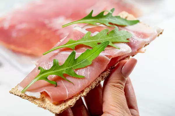 Diet sandwich with crispbread, dry-cured ham and arugula in women hand (Flip 2019)