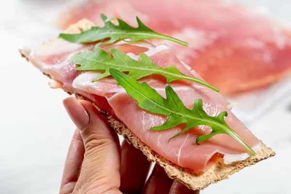 Diet sandwich with crispbread, dry-cured ham and arugula in women hand