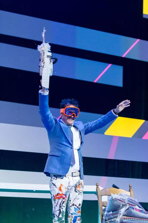 Dietmar Dahmen auf der Bühne mit einer roten Brille, einer Säge in der Hand und einer bunten Hose