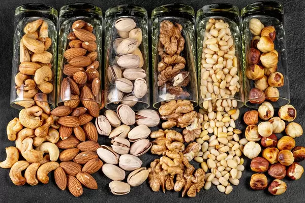 Different nuts poured from glasses on a black background (Flip 2020)