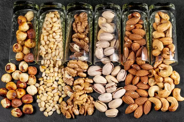 Different nuts poured from glasses on a black background