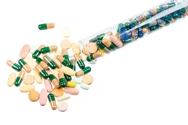 Different pills poured out of a test tube on a white background