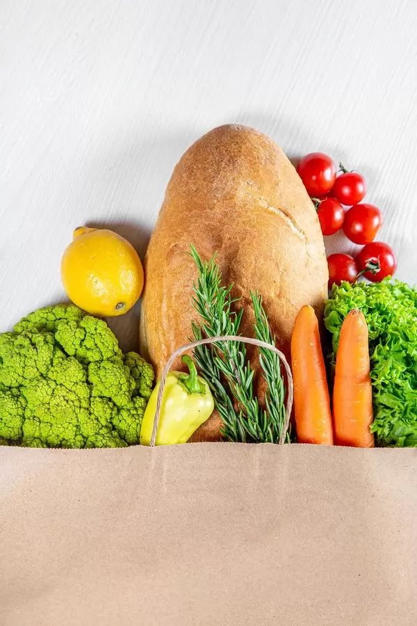 Different vegetables and bread in the paper bag over the white background