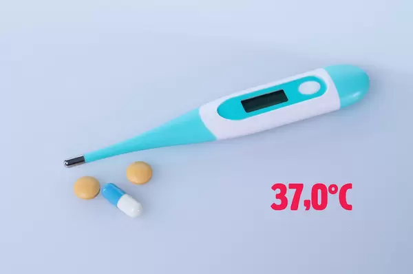 Digital thermometer with pills and 37°C text on light blue background