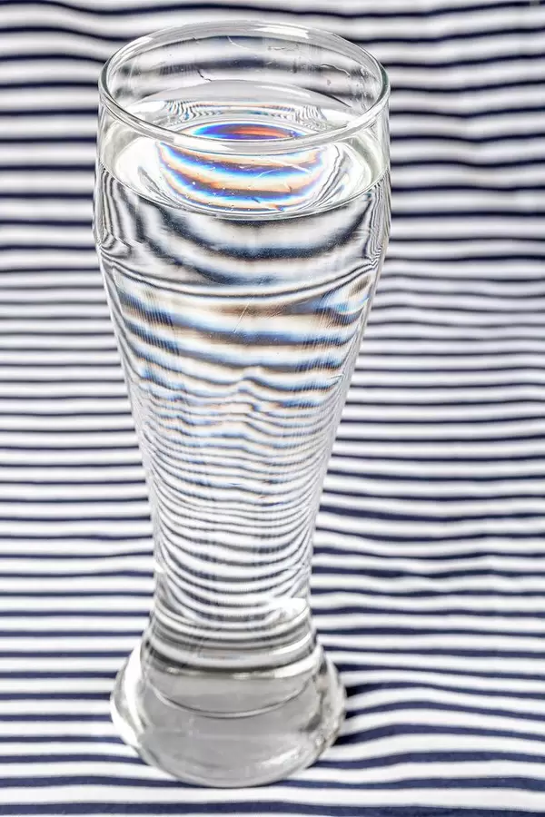 Distortion of white and black striped background with the help water in glass