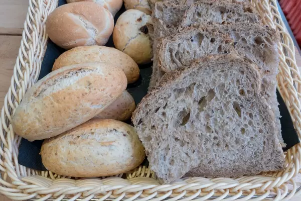 Diverse Brötchen und Brotscheiben in einem geflochtenen Brotkorb