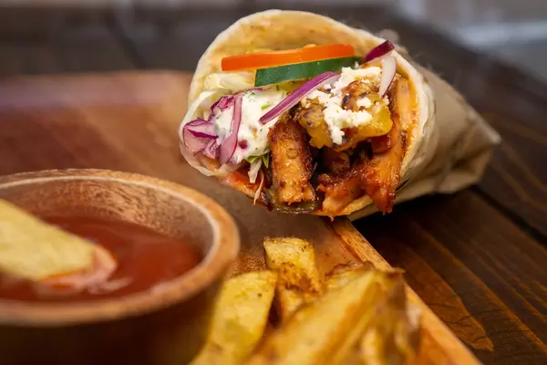 Döner Dürüm mit Hähnchenfleisch, Tzatziki Soße, Tomaten, Gurken, Feta Käse, Salat, Rotkohl und Zwiebeln neben Pommes Frites und Ketchup Nahaufnahme