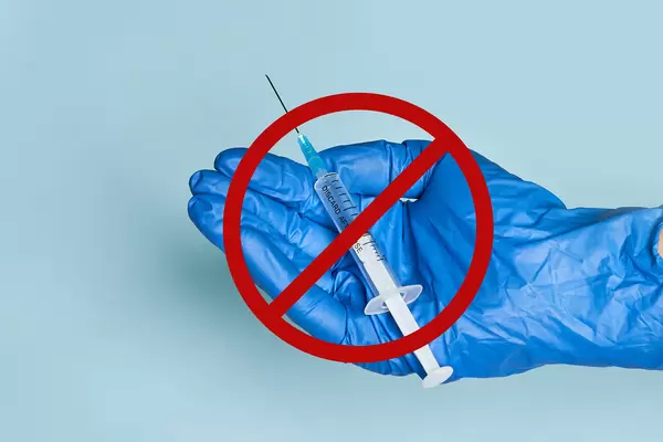 Doctor hands holding a syringe with vaccine shot and prohibited sign on it. Concept of anti vaccination, anti vaxxers movements